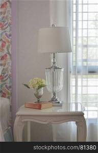 Crystal base reading lamp on white wooden bedside table with book and flower
