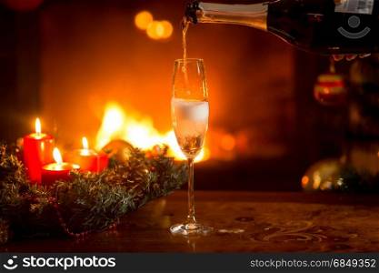 Crystal glass being filled with champagne. Burning fireplace and Christmas tree on the background