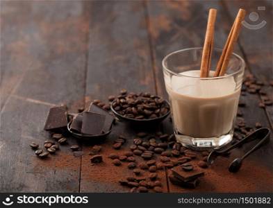 Crystal glass of Irish cream baileys liqueur with cinnamon, coffee beans and powder with dark chocolate on dark wood background. Space for text
