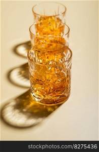 Crystal glasses of single malt whiskey with ice cubes on golden background.
