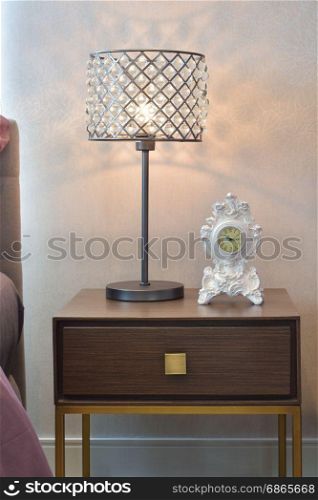 crystal reading lamp and classic clock on bedside table in cozy bedroom interior