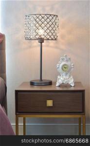 crystal reading lamp and classic clock on bedside table in cozy bedroom interior
