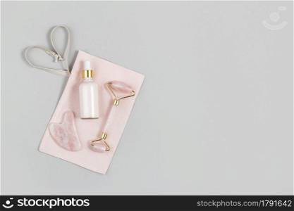 Crystal rose quartz facial roller, massage tool Gua sha and anti-aging collagen, serum in glass bottle on pink fabric bag, grey background. Facial massage for natural lifting, Beauty concept Top view.. Crystal rose quartz facial roller, massage tool Gua sha and anti-aging collagen, serum in glass bottle on pink fabric bag, grey background. Facial massage for natural lifting, Beauty concept Top view