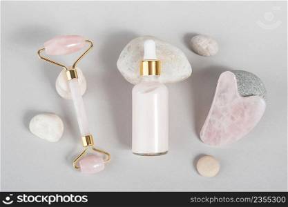 Crystal rose quartz facial roller, massage tool Gua sha and anti-aging collagen, serum in glass bottle on stones, grey background. Facial massage for natural lifting, Beauty concept. Top view.. Crystal rose quartz facial roller, massage tool Gua sha and anti-aging collagen, serum in glass bottle on stones, grey background. Facial massage for natural lifting, Beauty concept Top view