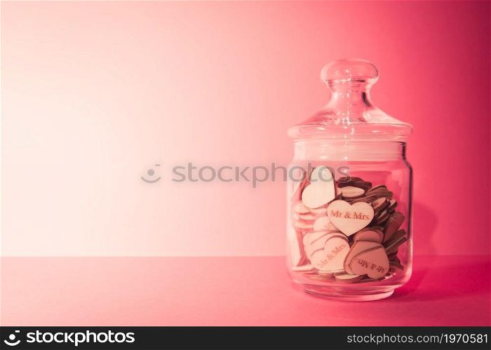 Crystal white bottle with wooden hearts in it over a pastel pink background with copy space