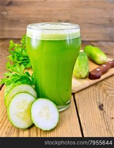 Cucumber juice in a tall glass, cucumbers and parsley, knife on a wooden boards background