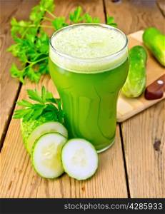 Cucumber juice in a tall glass, cucumbers, parsley and knife on a wooden boards background