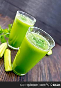 Cucumber juice in two tall glasses, cucumber and parsley on a dark wooden board