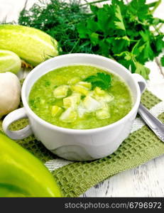 Cucumber soup with green peppers and garlic in a bowl on a napkin, parsley on a wooden boards background