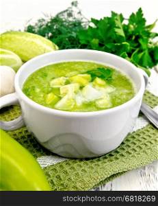 Cucumber soup with green peppers and garlic in a bowl on a napkin, parsley on the background light wooden boards