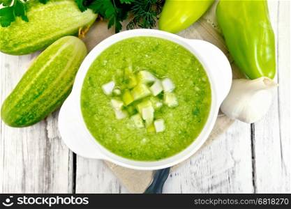 Cucumber soup with green peppers and garlic in a bowl on a napkin, parsley on a background of wooden boards on top