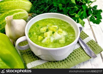 Cucumber soup with green peppers and garlic in a bowl on green napkin, parsley on a wooden boards background