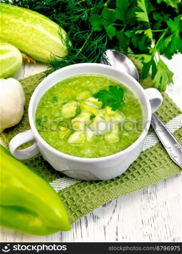 Cucumber soup with green peppers and garlic in a white bowl on a napkin, parsley on a wooden boards background