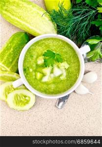 Cucumber soup with green peppers and garlic in a white bowl, parsley on a background of a granite table top