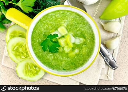 Cucumber soup with green peppers and garlic in a yellow bowl, parsley on a background of a granite table top