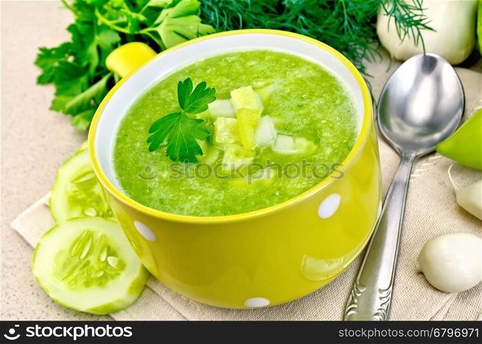 Cucumber soup with green peppers and garlic in a yellow bowl, parsley on a background of a granite table