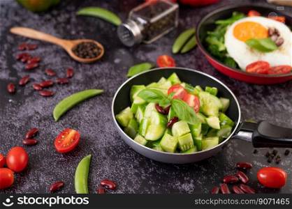 Cucumber stir-fried with tomatoes and red beans in a frying pan with green peas Pepper seeds on black cement.
