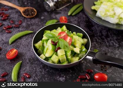 Cucumber stir-fried with tomatoes and red beans in a frying pan with green peas Pepper seeds on black cement.