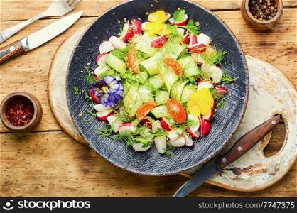 Cucumber,tomato,radish and greens salad decorated with edible flowers.Spring vitamin salad. Seasonal vegetable salad on rustic wooden table