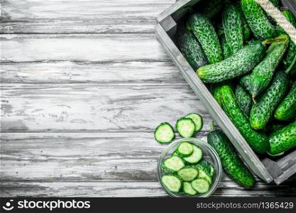 Cucumbers in the box and cucumber slices in the bowl. On wooden background. Cucumbers in the box and cucumber slices in the bowl.