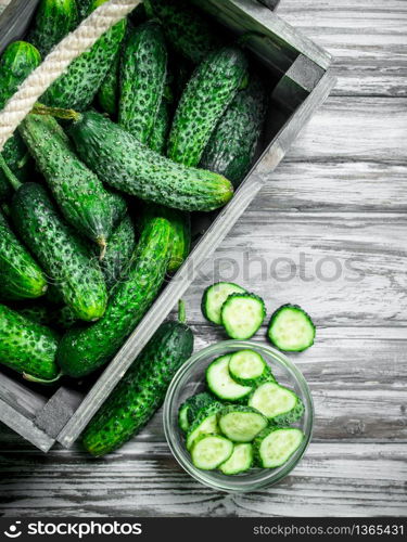 Cucumbers in the box and cucumber slices in the bowl. On wooden background. Cucumbers in the box and cucumber slices in the bowl.