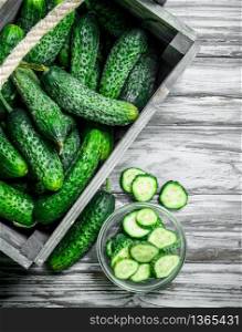 Cucumbers in the box and cucumber slices in the bowl. On wooden background. Cucumbers in the box and cucumber slices in the bowl.