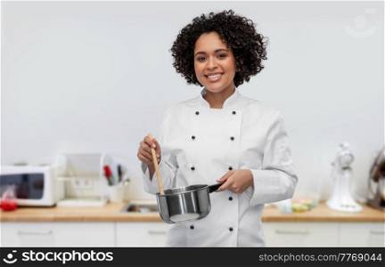 culinary and people concept - happy smiling female chef in jacket with saucepan cooking food over restaurant kitchen background. happy smiling female chef with saucepan on kitchen