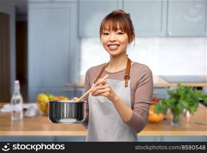 culinary and people concept - happy smiling female chef in jacket with saucepan cooking food over home kitchen background. happy smiling female chef with saucepan in kitchen