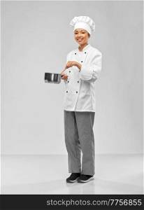 culinary and people concept - happy smiling female chef in toque and jacket with saucepan cooking food over grey background. happy smiling female chef with saucepan