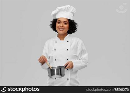 culinary and people concept - happy smiling female chef in toque with saucepan cooking food over grey background. female chef with saucepan and spoon cooking food