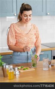 culinary and people concept - happy smiling young woman making cocktail drinks with lime and peppermint at home kitchen. woman making cocktail drinks at home kitchen