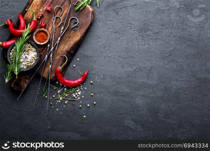 Culinary background with a space for a text. Flat lay composition of chili peppers, rosemary, spices and skewers for shish kebab on a black surface, top view