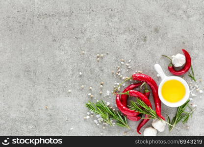 Culinary background with a space for a text, flat lay composition of oil, chili peppers, rosemary, garlic and spices on a table stone surface, top view