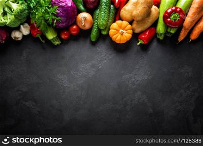 Culinary background with fresh raw vegetables on a black kitchen table, healthy vegetarian food concept, flat lay composition, top view