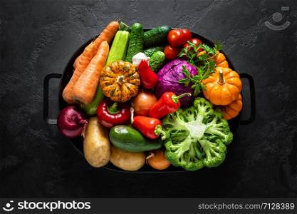 Culinary background with fresh raw vegetables on a black kitchen table, healthy vegetarian food concept, flat lay composition, top view