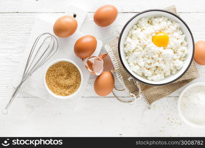 Culinary background with ingredients for cooking, cottage cheese, baking flour, sugar and eggs on white wooden rustic table, top view