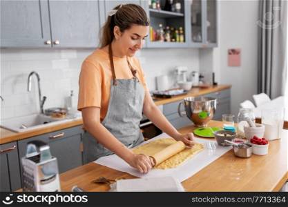 culinary, bake and people concept - happy smiling young woman cooking food on kitchen at home rolls dough with rolling pin. woman cooking food and baking on kitchen at home