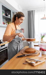 culinary, baking and cooking food concept - happy smiling young woman making layer cake on kitchen at home. woman cooking food and baking on kitchen at home