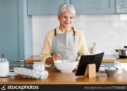 culinary, baking and people concept - happy smiling woman with cook book cooking food on kitchen at home. happy woman with cook book cooking food on kitchen