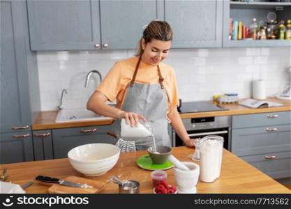 culinary, baking and people concept - happy smiling young woman cooking food on kitchen at home adding sugar to bowl. woman cooking food and baking on kitchen at home