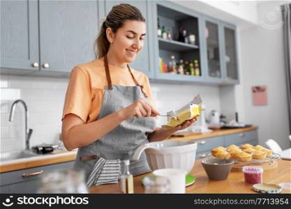 culinary, baking and people concept - happy smiling young woman cooking food on kitchen at home adding butter to bowl. woman cooking food and baking on kitchen at home