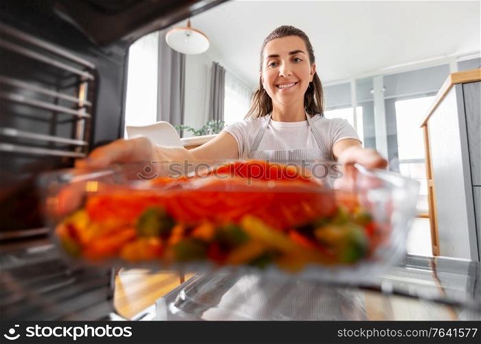 culinary, food and people concept - woman cooking salmon fish with vegetables in baking dish in oven at home kitchen. woman cooking food in oven at home kitchen