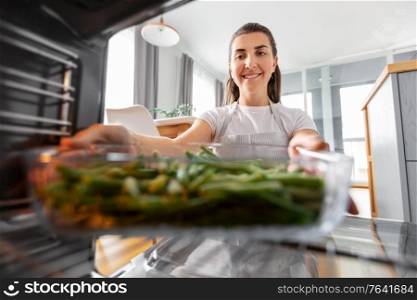 culinary, food and people concept - woman cooking vegetables in baking dish in oven at home kitchen. woman cooking food in oven at home kitchen