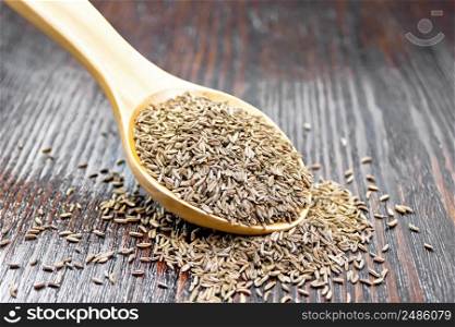 Cumin seeds in a spoon on a brown wooden board background