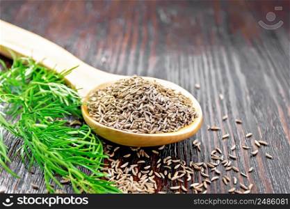 Cumin seeds in spoon and on the table, a green sprig of caraway on the background of wooden board