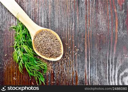Cumin seeds in spoon and on the table, a green twig of a plant on background of wooden board from above