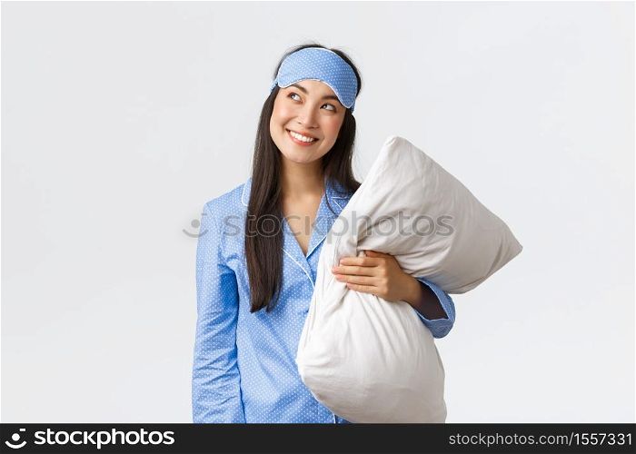 Cunning and thoughtful kawaii asian girl in blue pajama and sleeping mask, holding pillow and looking curious upper left corner, smiling sly as having idea, imaging something, white background.. Cunning and thoughtful kawaii asian girl in blue pajama and sleeping mask, holding pillow and looking curious upper left corner, smiling sly as having idea, imaging something, white background