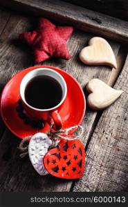 Cup decorated with wooden hearts. Red Cup with black coffee and two carved decorative wooden heart.Selective focus
