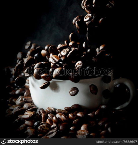 Cup filled with falling hot fresh steaming coffee beans on black. Falling coffee beans in white cup