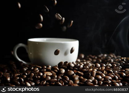 Cup filled with hot fresh steaming coffee beans on black